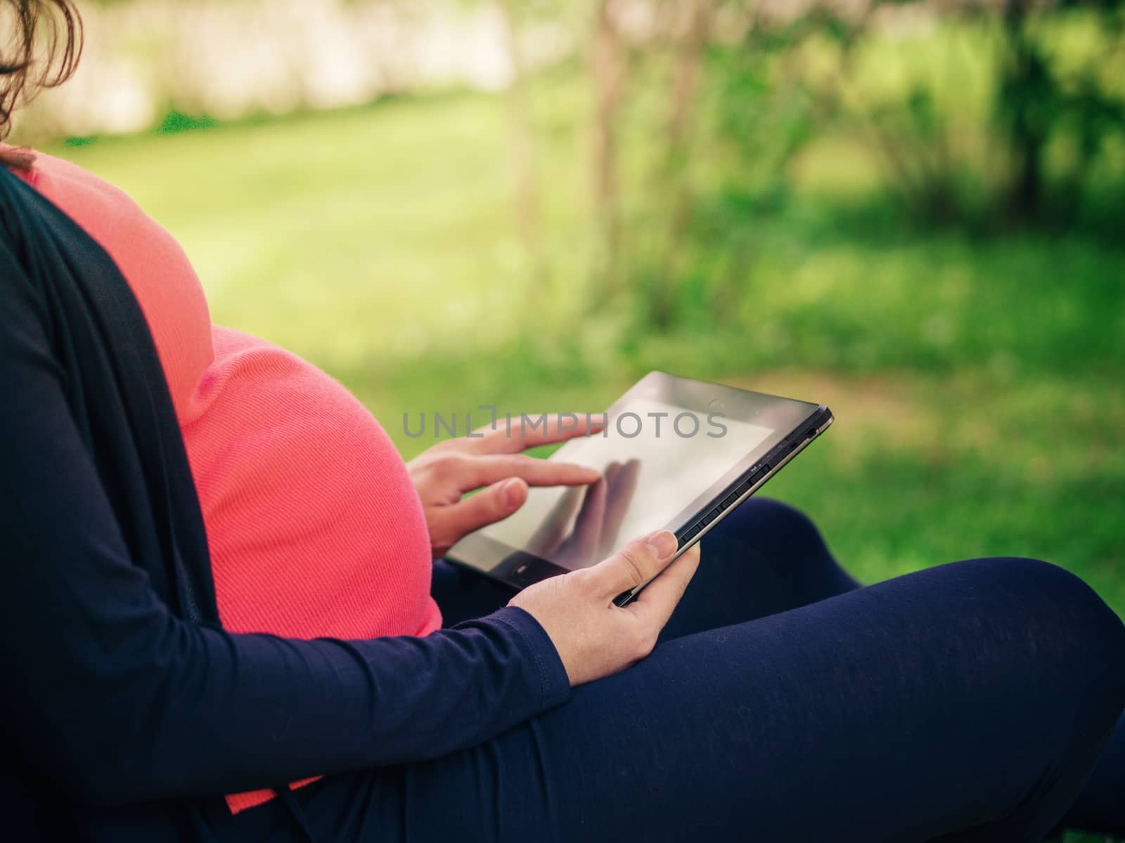 Close up view of pregnant belly and tablet pc. Pregnancy outdoors concept. Copy space.