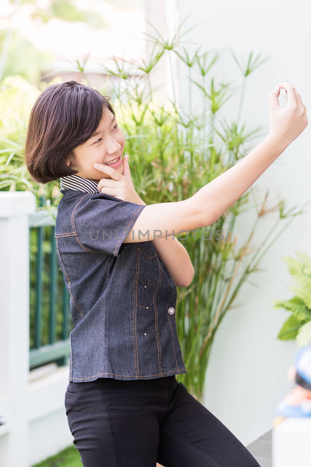 Asian girl with short hair using mobile phone to take selfie outdoor in garden