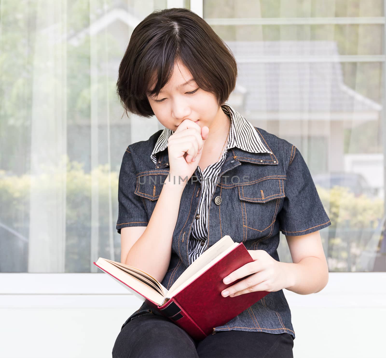 Young woman reading book sitting on chair  by stoonn