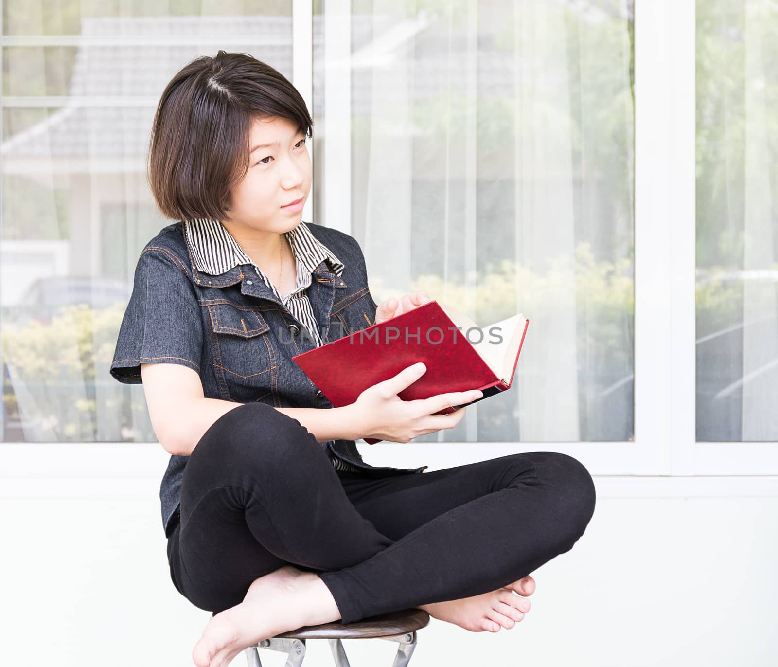 Young woman reading book sitting on chair  by stoonn