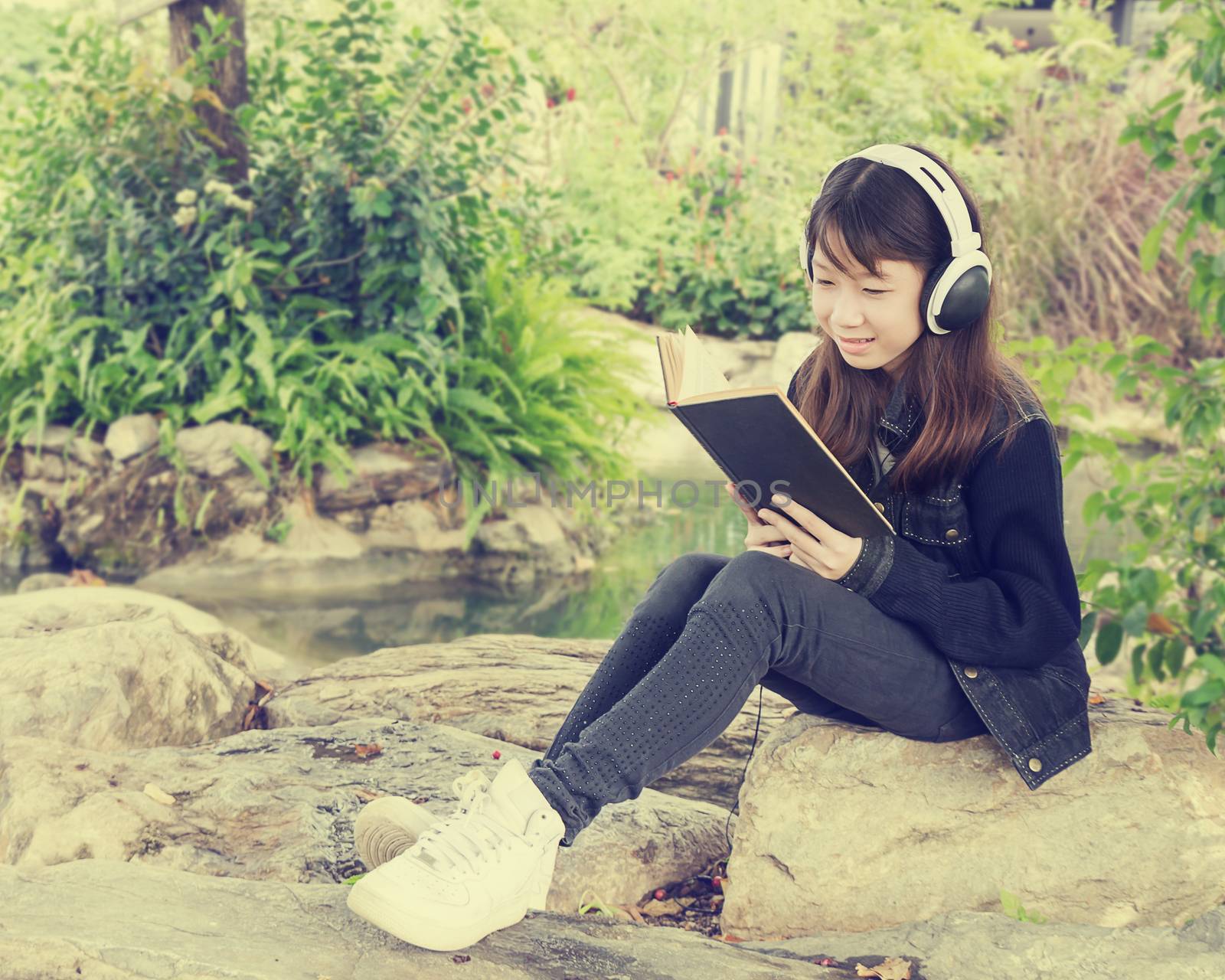 Young beautiful girl reading a book and 
listen to music in the park