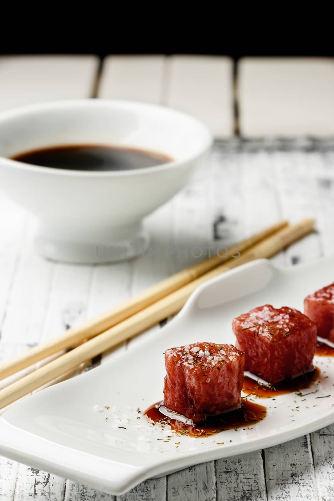 Tuna sashimi dipped in soy sauce,  thick salt and dill on old white wooden board with chopsticks and sauce bowl. Raw fish in traditional Japanese style. Vertical image.