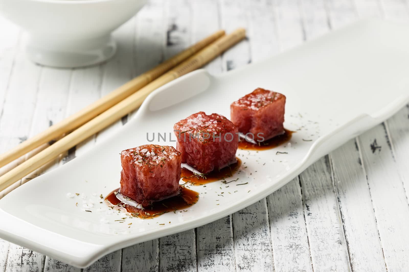 Tuna sashimi dipped in soy sauce,  thick salt and dill on old white wooden board with chopsticks and sauce bowl. Raw fish in traditional Japanese style. Horizontal image.