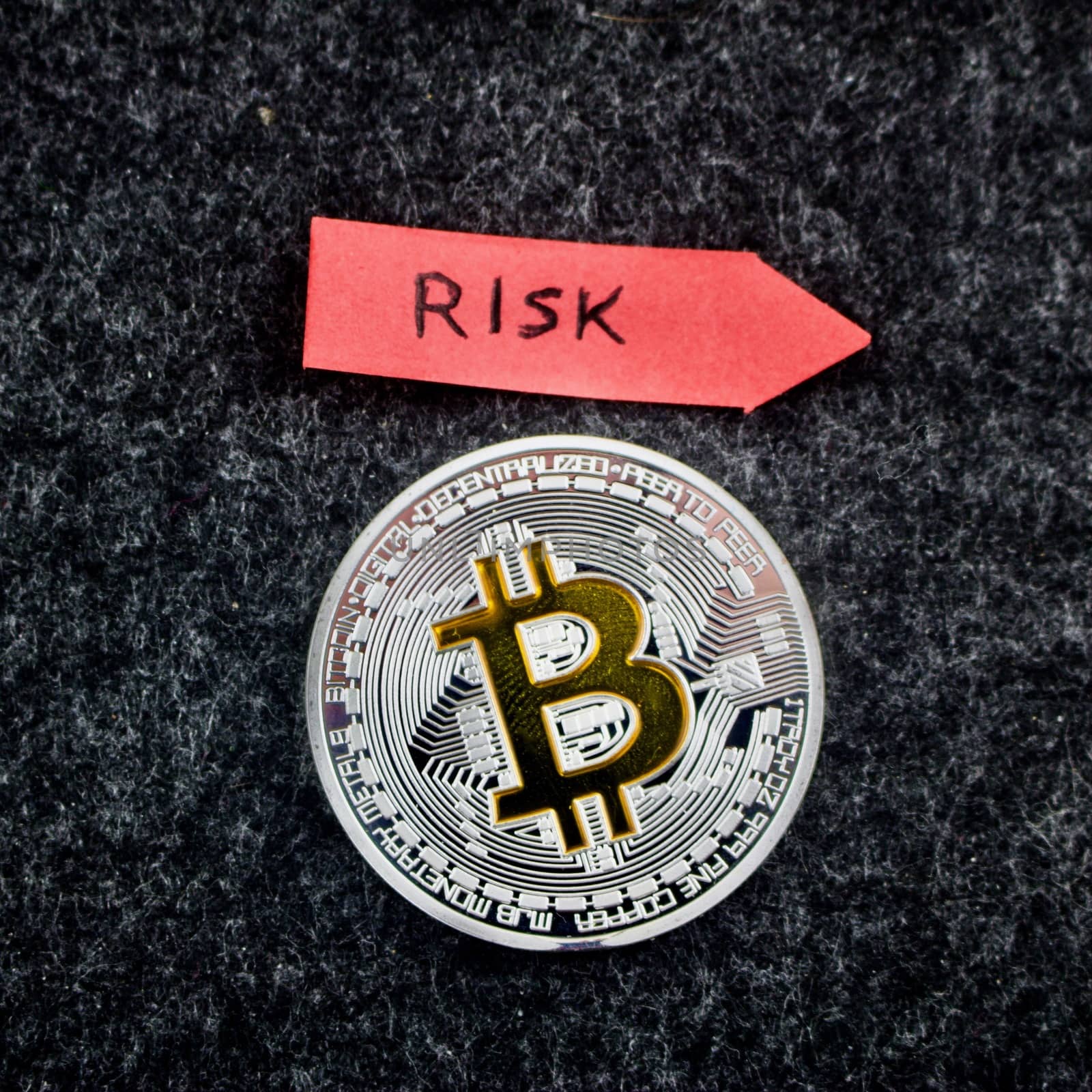 Cryptocurrency physical silver bitcoin coin and red arrow with risk inscription