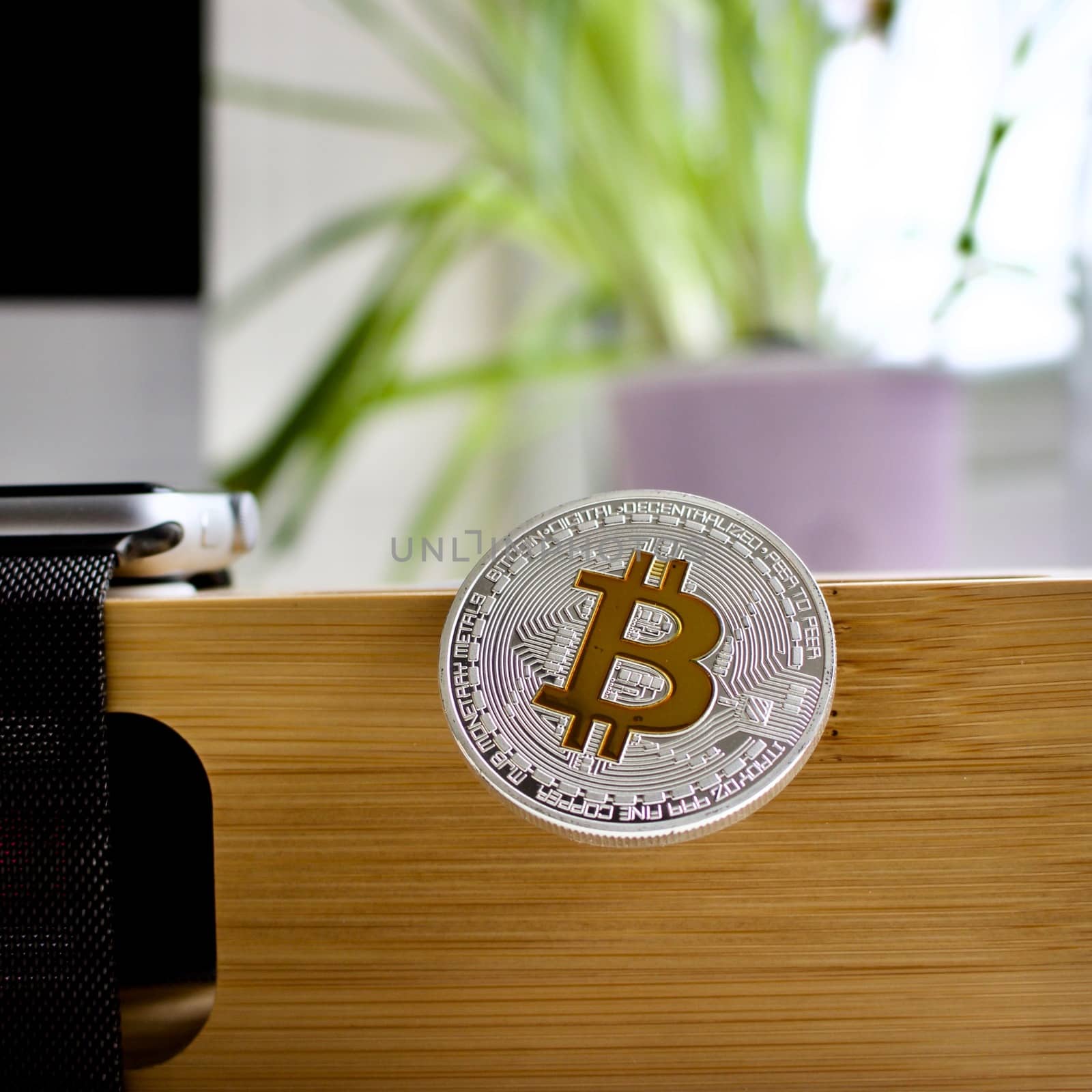 Cryptocurrency physical silver bitcoin coin on the wooden holder near watch.