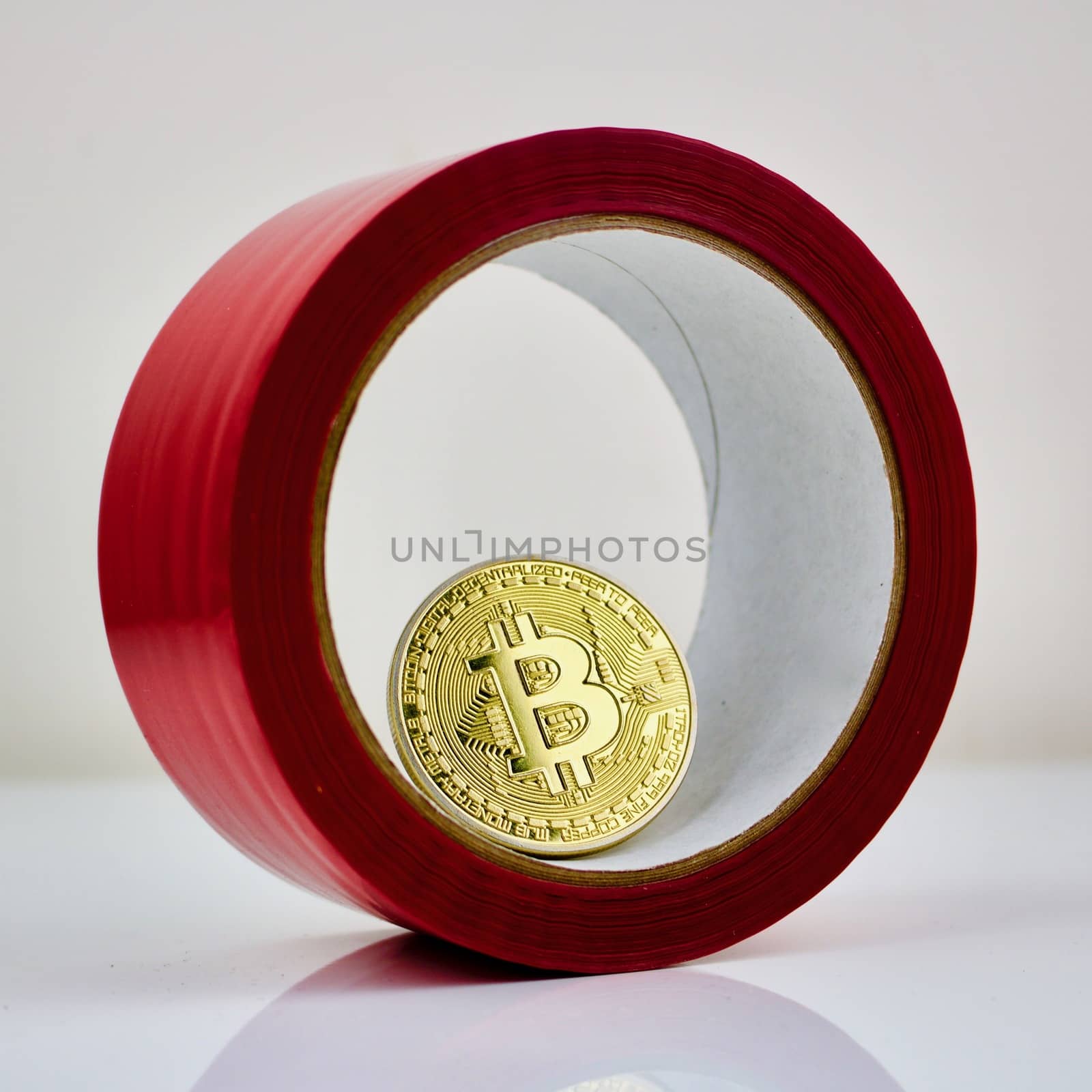 Physical gold bitcoin cryptocurrency coin inside red glue tape.