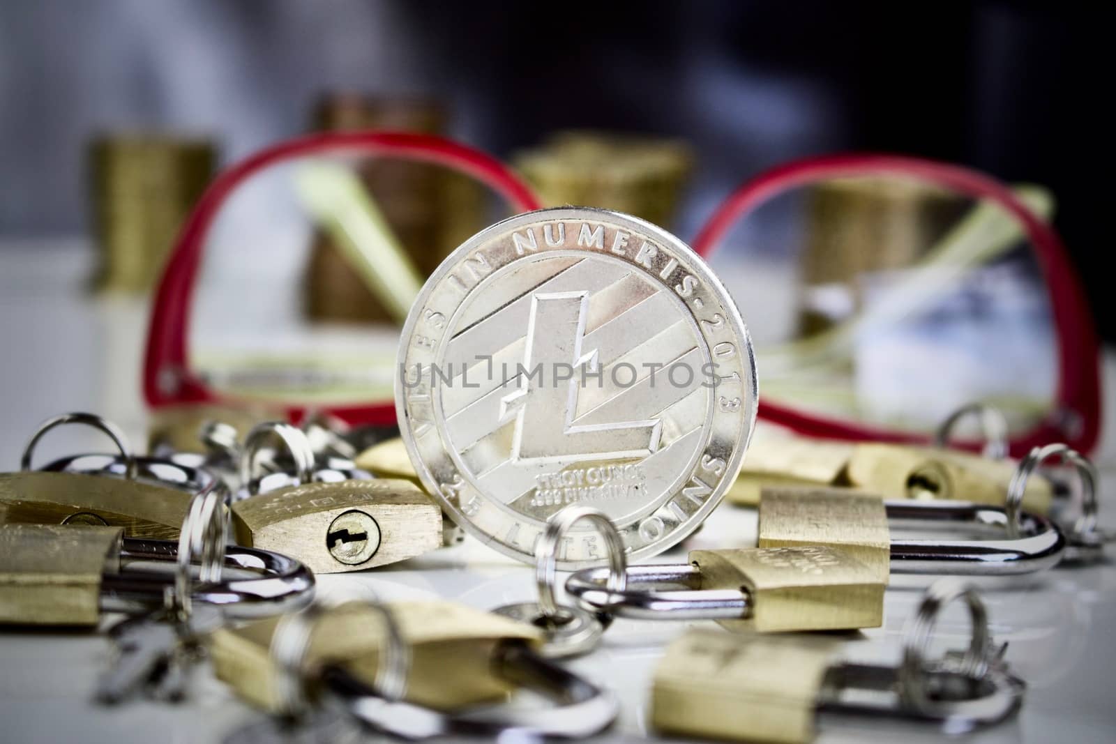 Cryptocurrency physical silver litecoin coin near gold padlocks and pink glasses