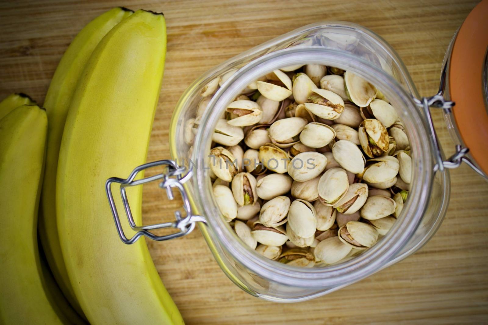 Pistachio nuts in jar and yellow bananas on the wooden board