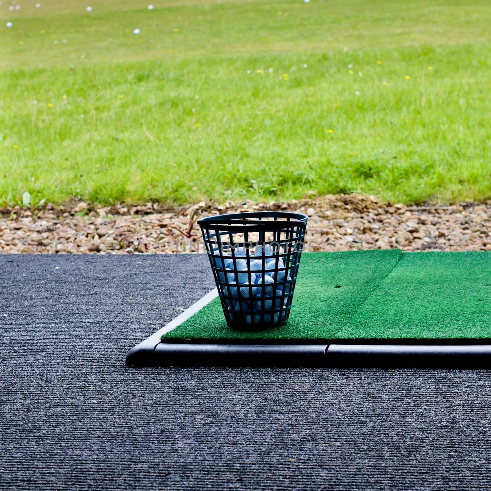 White golf balls in plastic basket on the green fake grass.