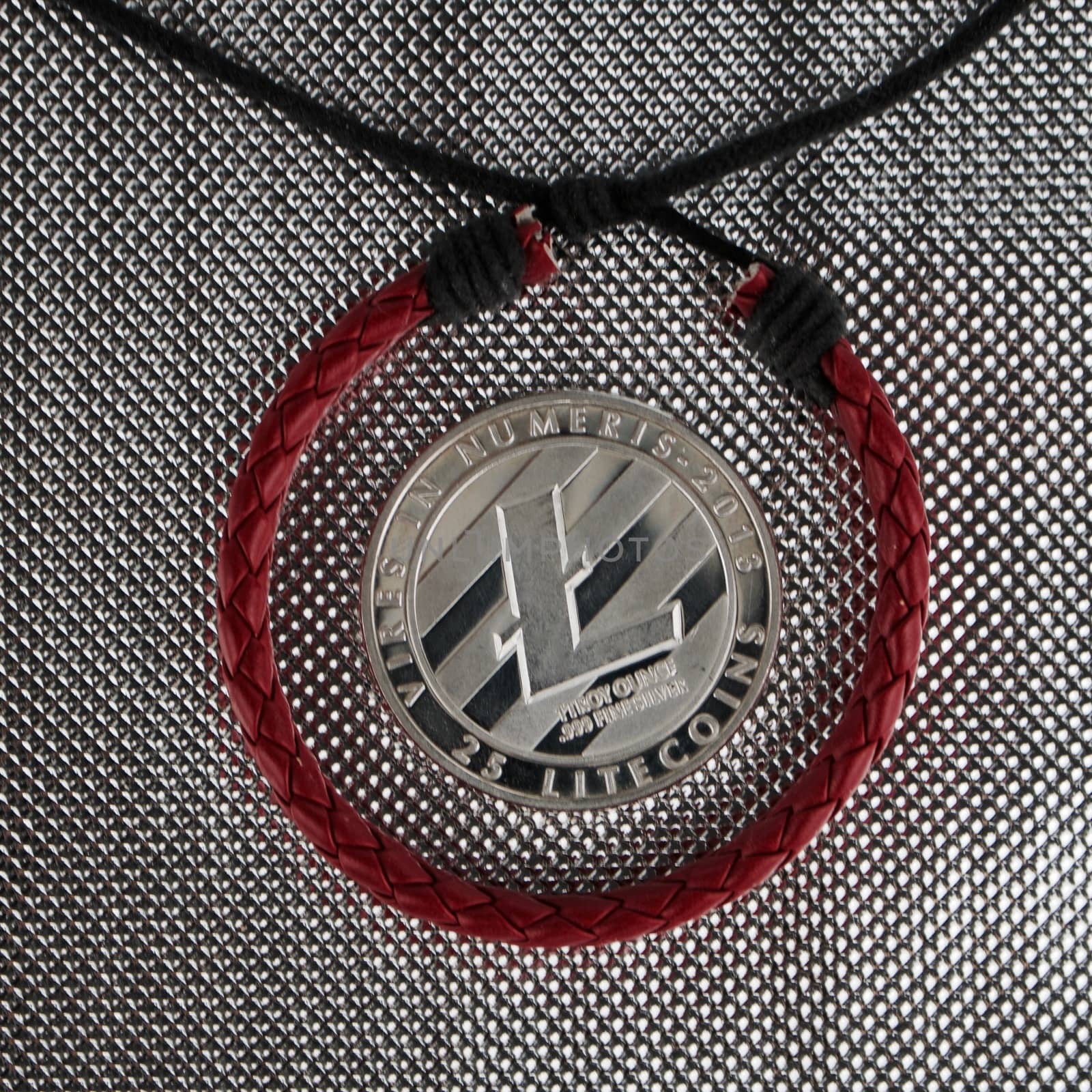 Cryptocurrency physical silver litecoin coin near red skin bracelet. Finance concept.