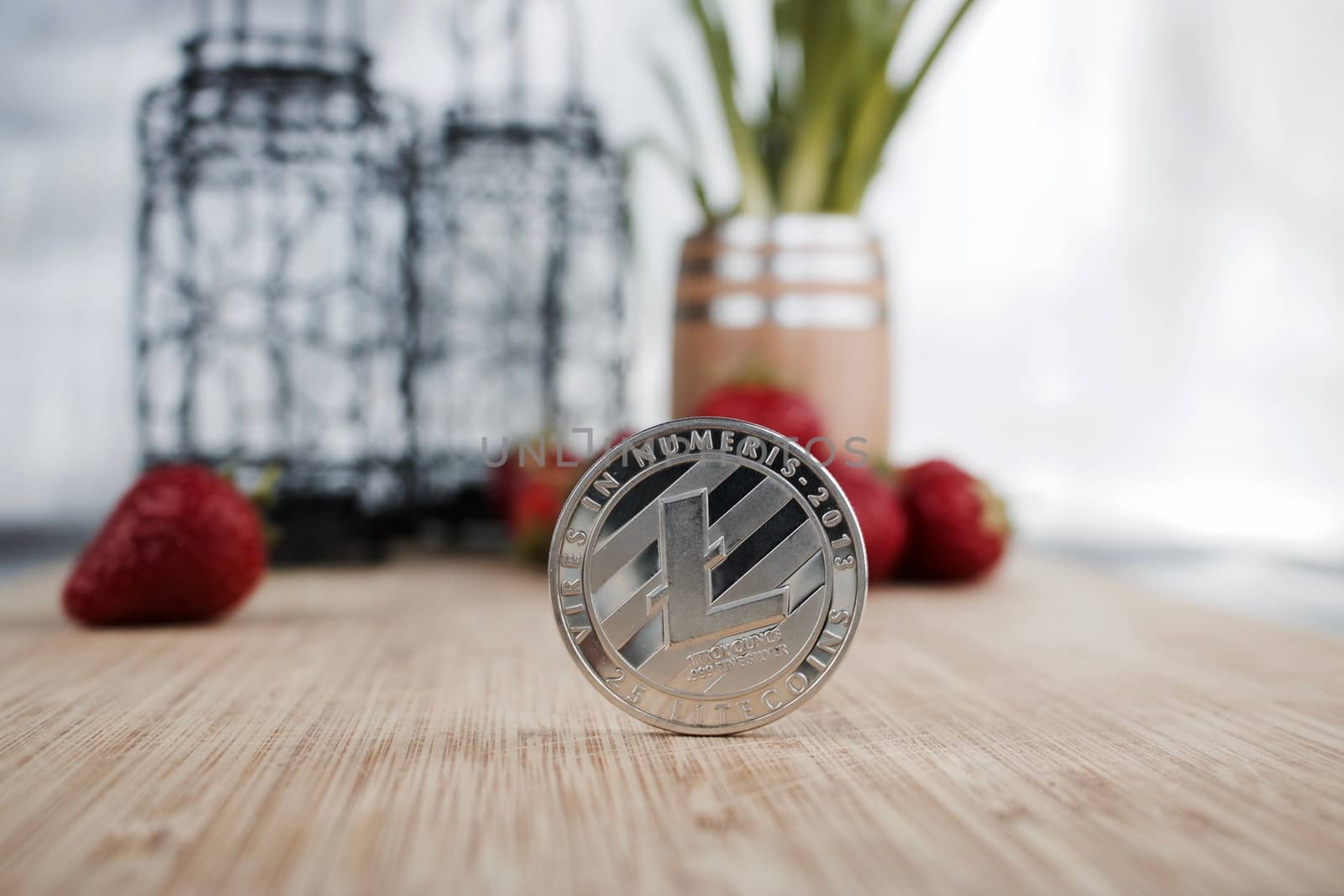 Digital currency silver Litecoin coin near strawberries.