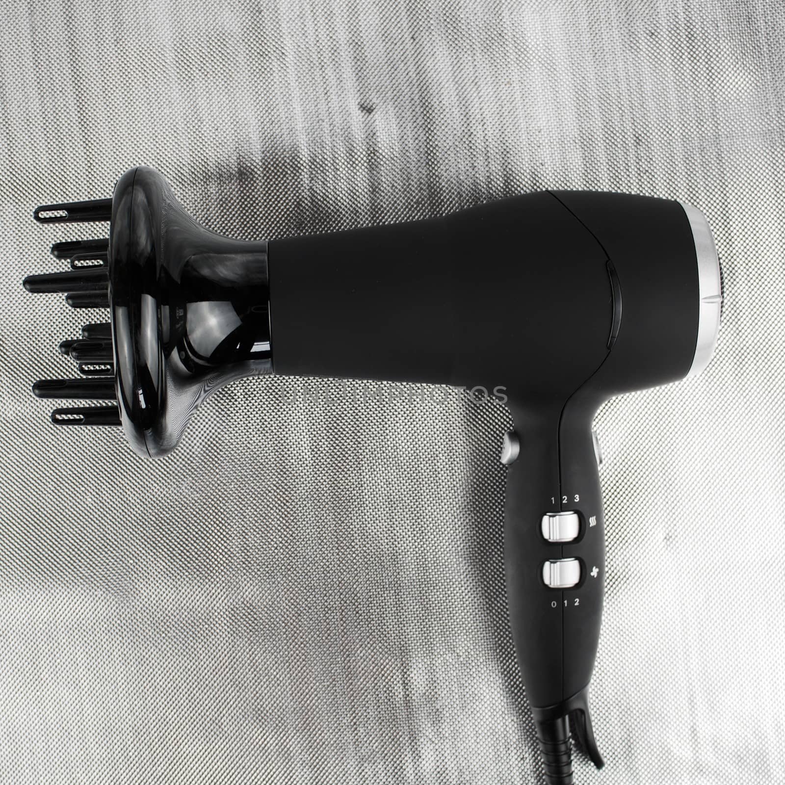 Big black proffesional hair dryer on the silver background with a silver buttons.