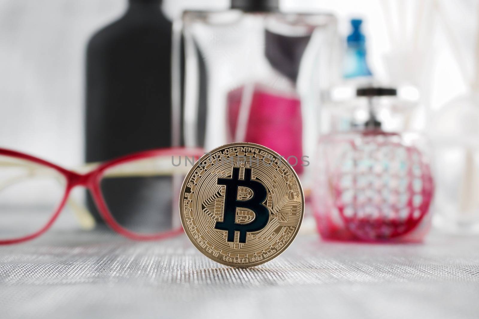 Digital currency physical gold bitcoin coin near pink glasses and fragnances
