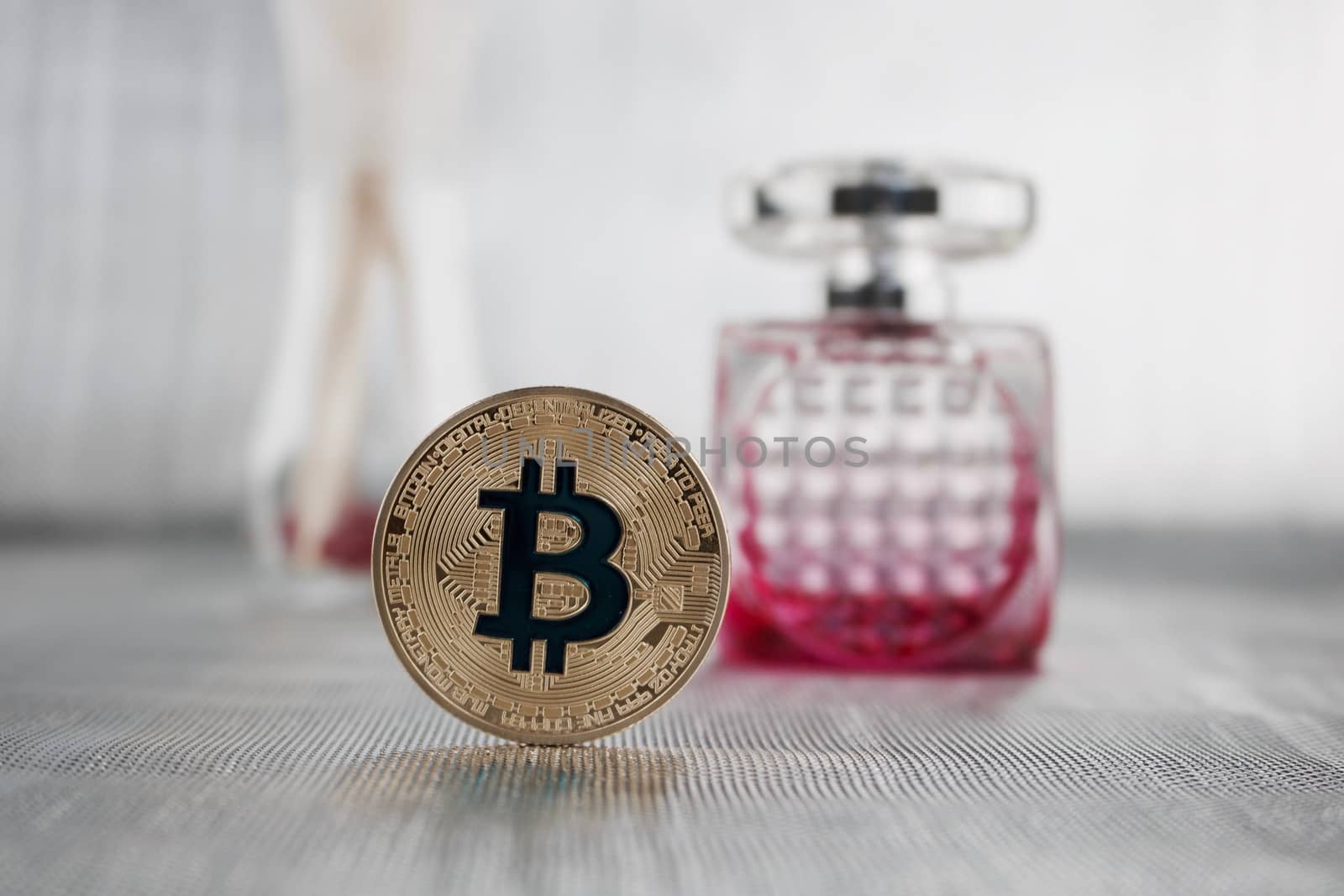 Cryptocurrency physical gold bitcoin coin near pink perfumes.