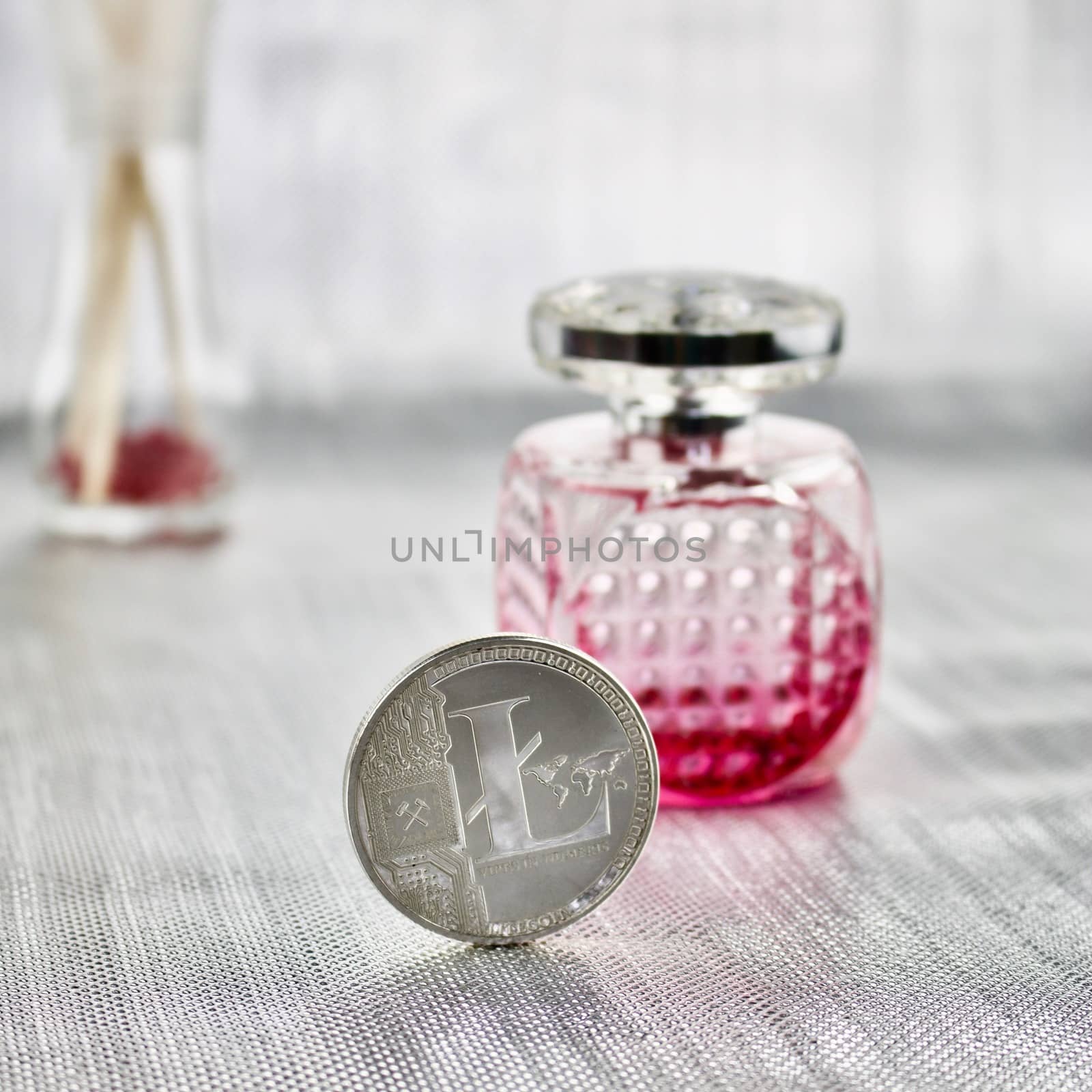 Digital currency physical silver litecoin coin near pink fragrance bottle.