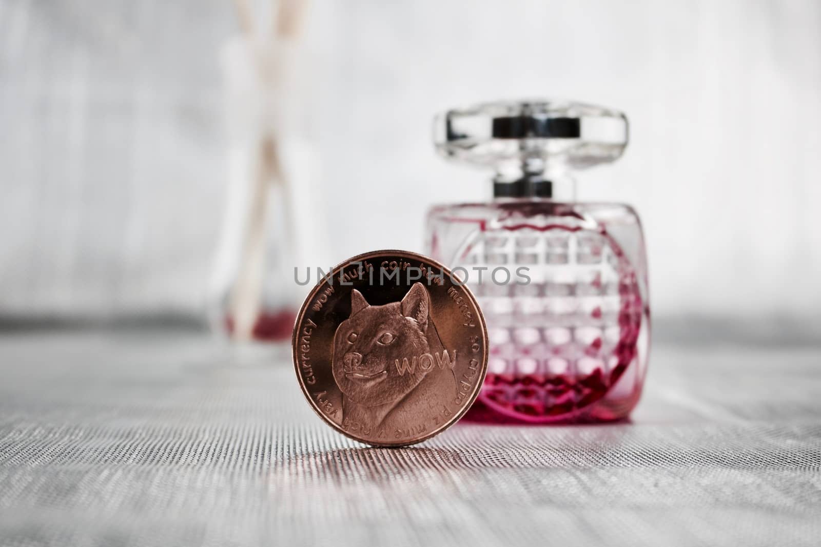 Digital currency physical brass doge coin near pink fragrance bottle.
