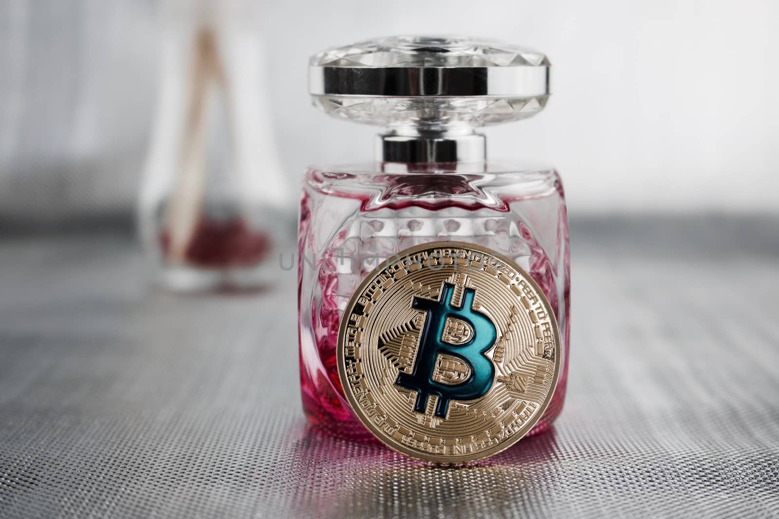 Cryptocurrency physical gold bitcoin coin near pink fragrance bootle.
