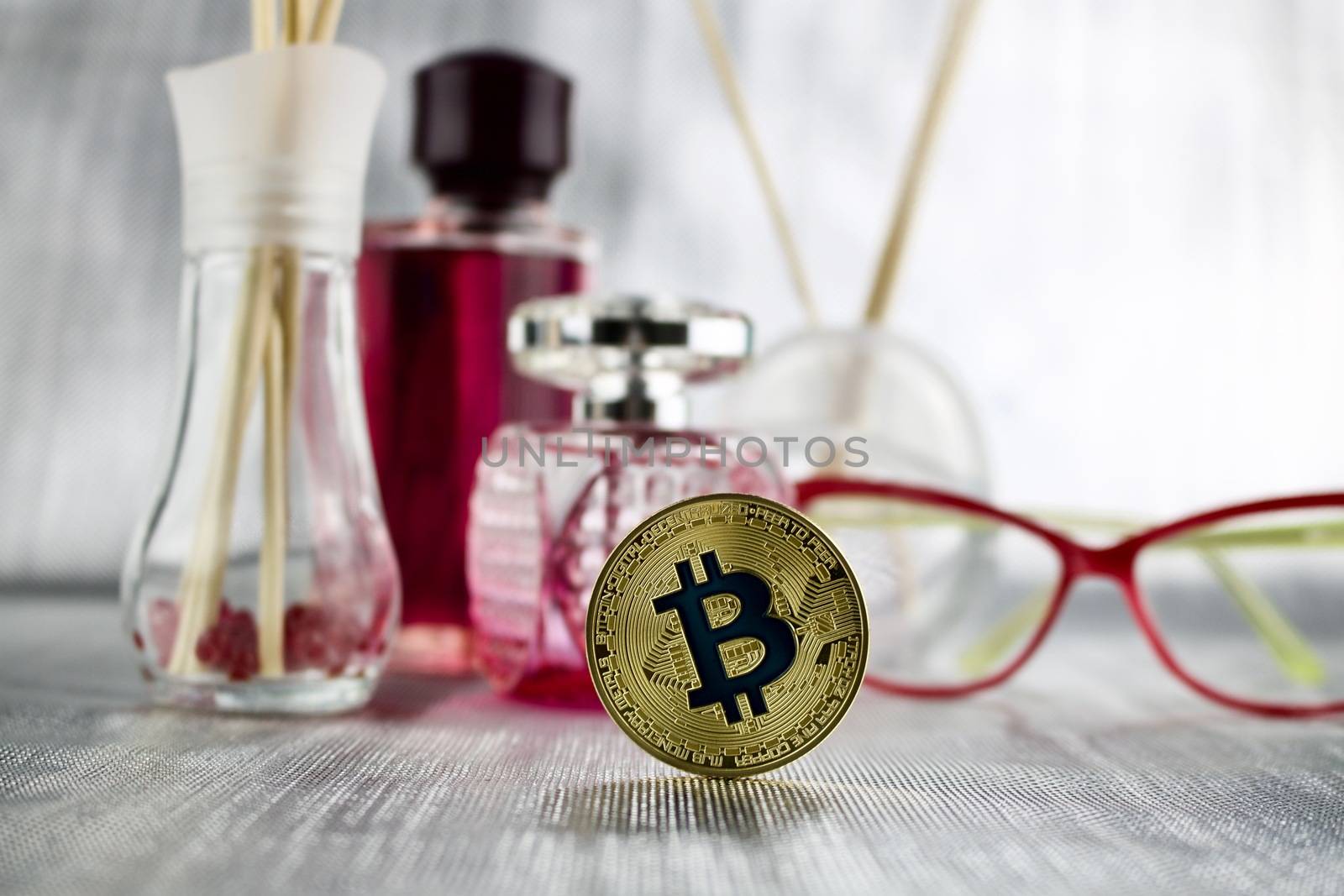 Cryptocurrency physical gold bitcoin coin near pink perfume and glasses