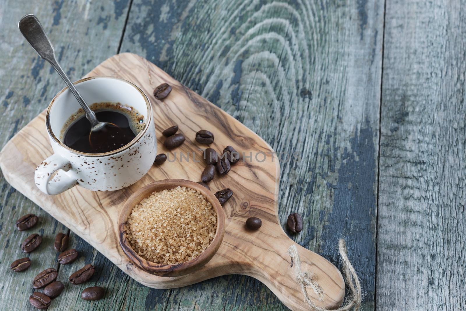 Black coffee in old coffee cup with a silver teaspoon, spilled coffee beans and cane sugar in a wooden bowl on the old wooden table