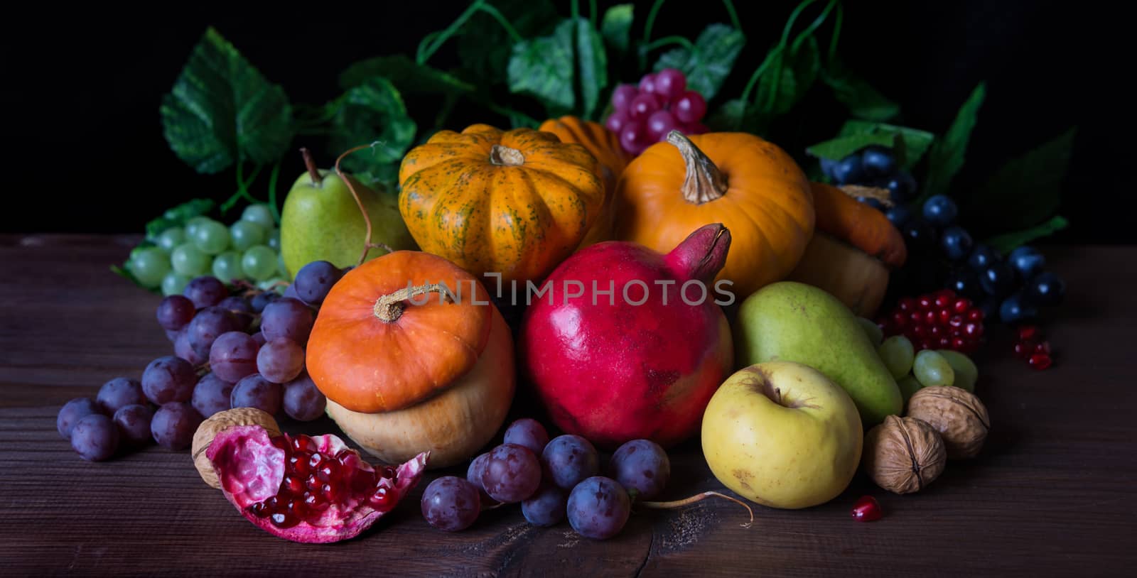 Autumn still life: decorative pumpkins, squash, apples, pears, pomegranates and grapes on the dark wooden background