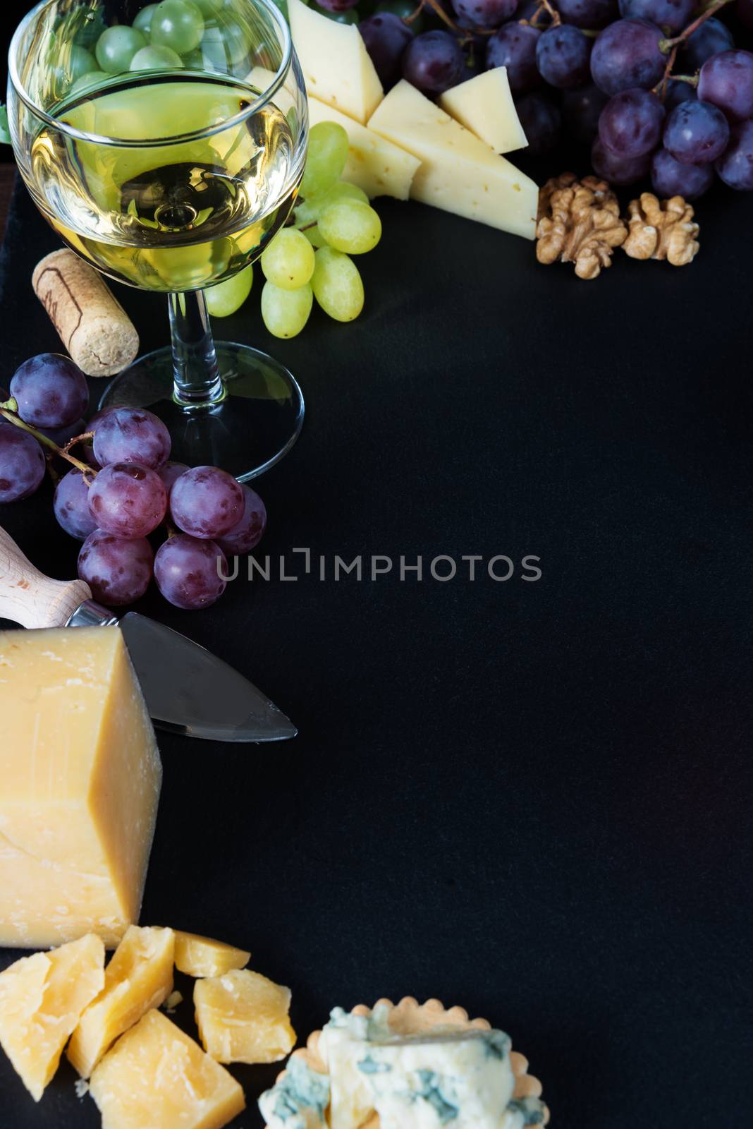 White wine, various types of cheese, walnuts and grapes on a black slate stone background