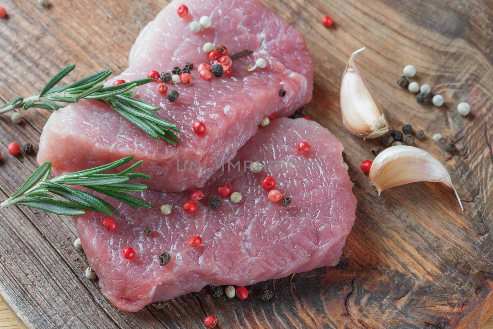 Two steaks from fresh organic meat and sprigs of rosemary on an old wooden board close up