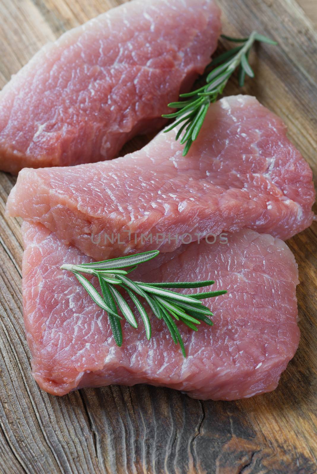 Three steaks of fresh organic meat and two sprigs of rosemary on an old wooden background closeup