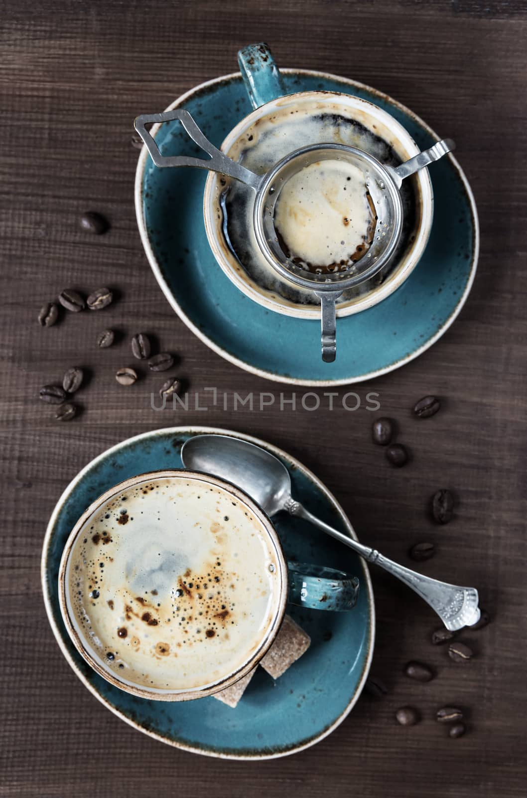 Two cups of coffee, coffee beans, pieces of sugar and teaspoons on a wooden table; top view