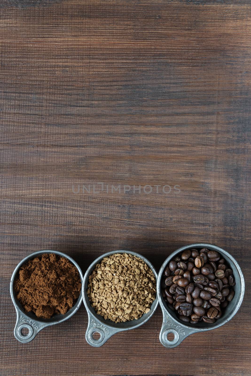 Coffee beans, instant coffee and ground coffee in a metal measuring cup on dark wooden background with copy-space, top view