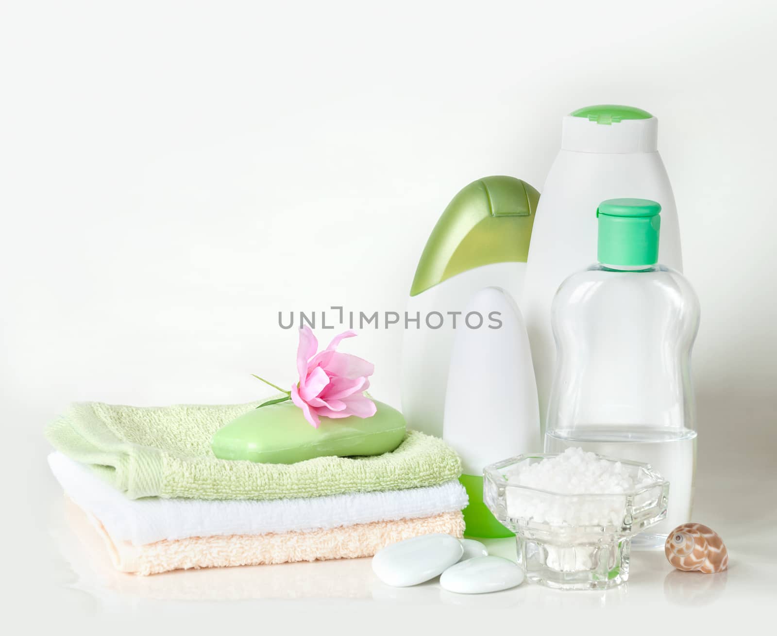 Green and white containers with different cosmetics, soap and a stack of towels, isolated on white background