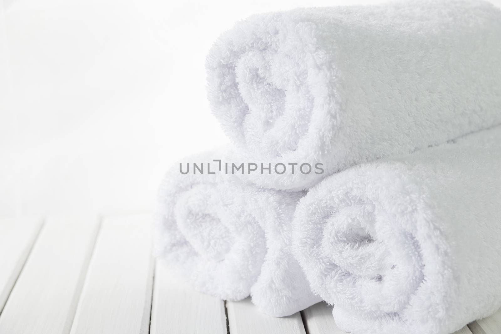 Stack of three rolls of white fluffy bath towels on the background of white boards