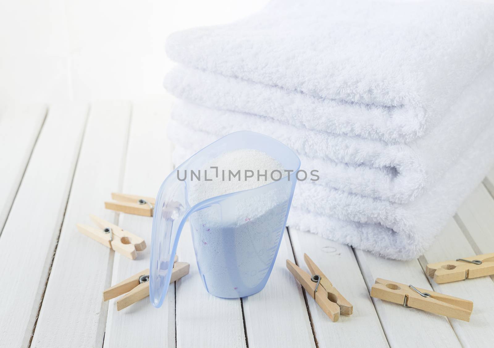 Stack of three white fluffy bath towels, washing powder in measuring cup and wooden clothespins on the background of white boards