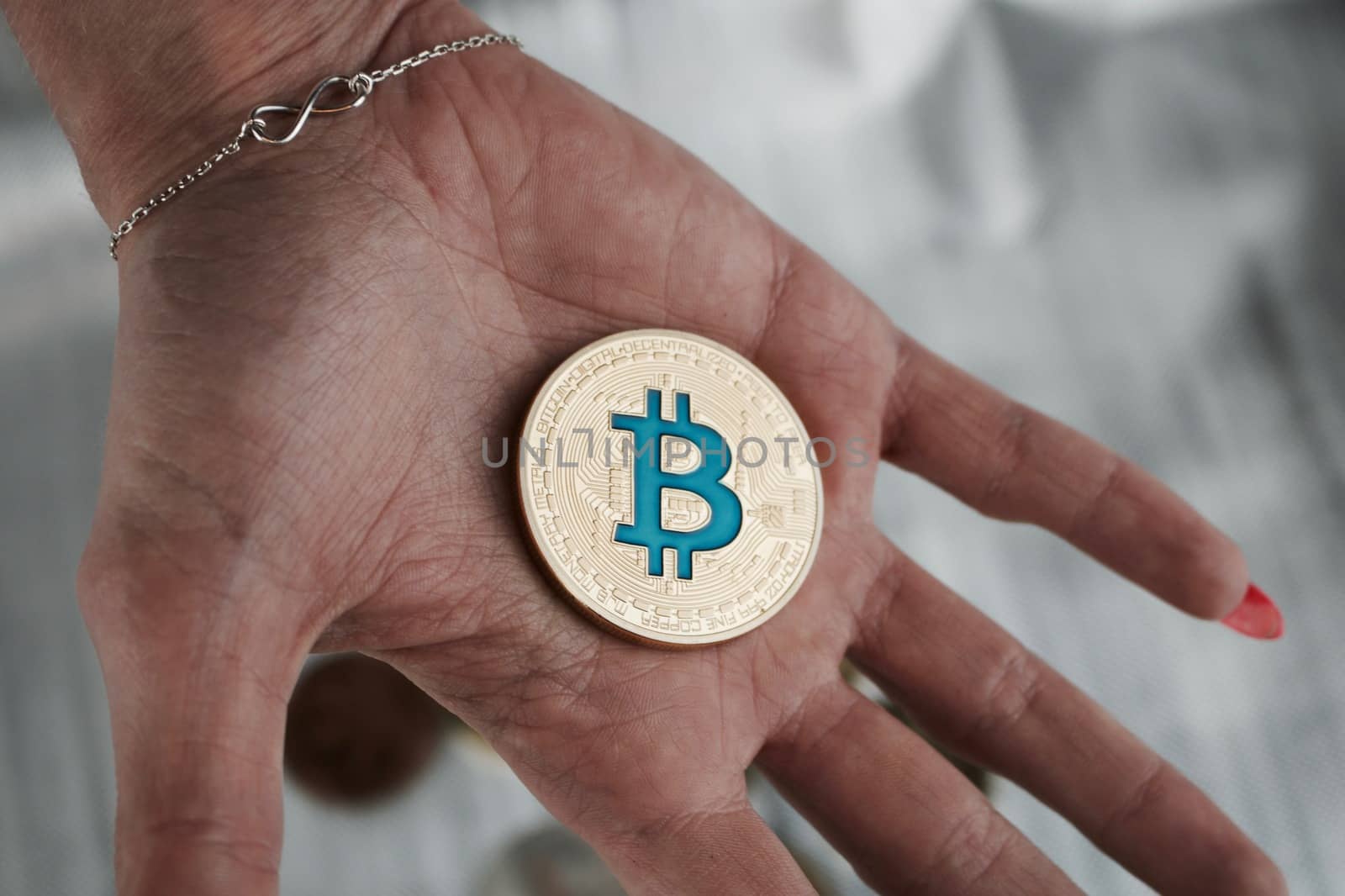 Cryptocurrency physical gold bitcoin coin on hand near infinity sign.