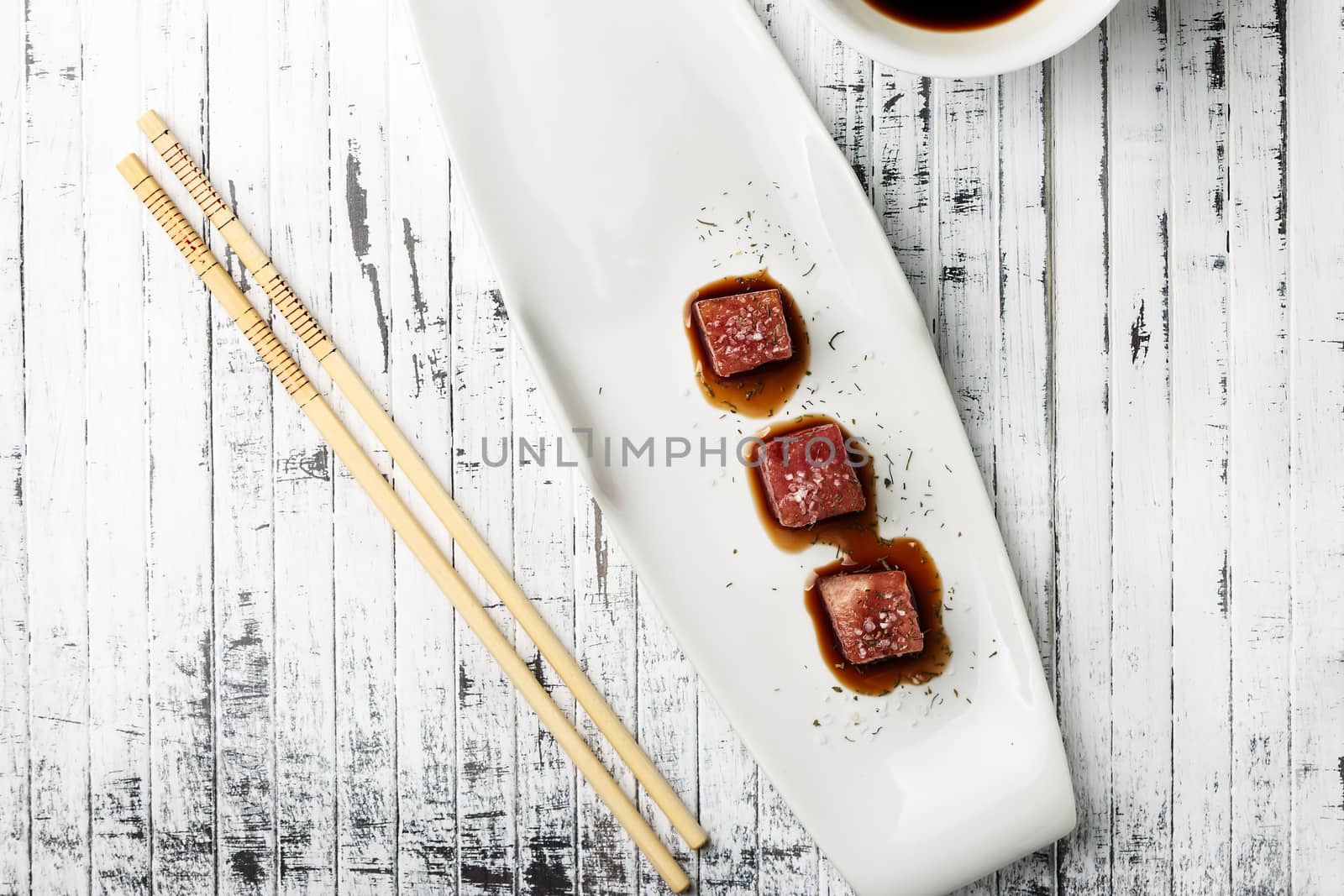 Tuna sashimi dipped in soy sauce,  thick salt and dill on old white wooden board with chopsticks and sauce bowl. Viewed from above. Raw fish in traditional Japanese style. Horizontal image.