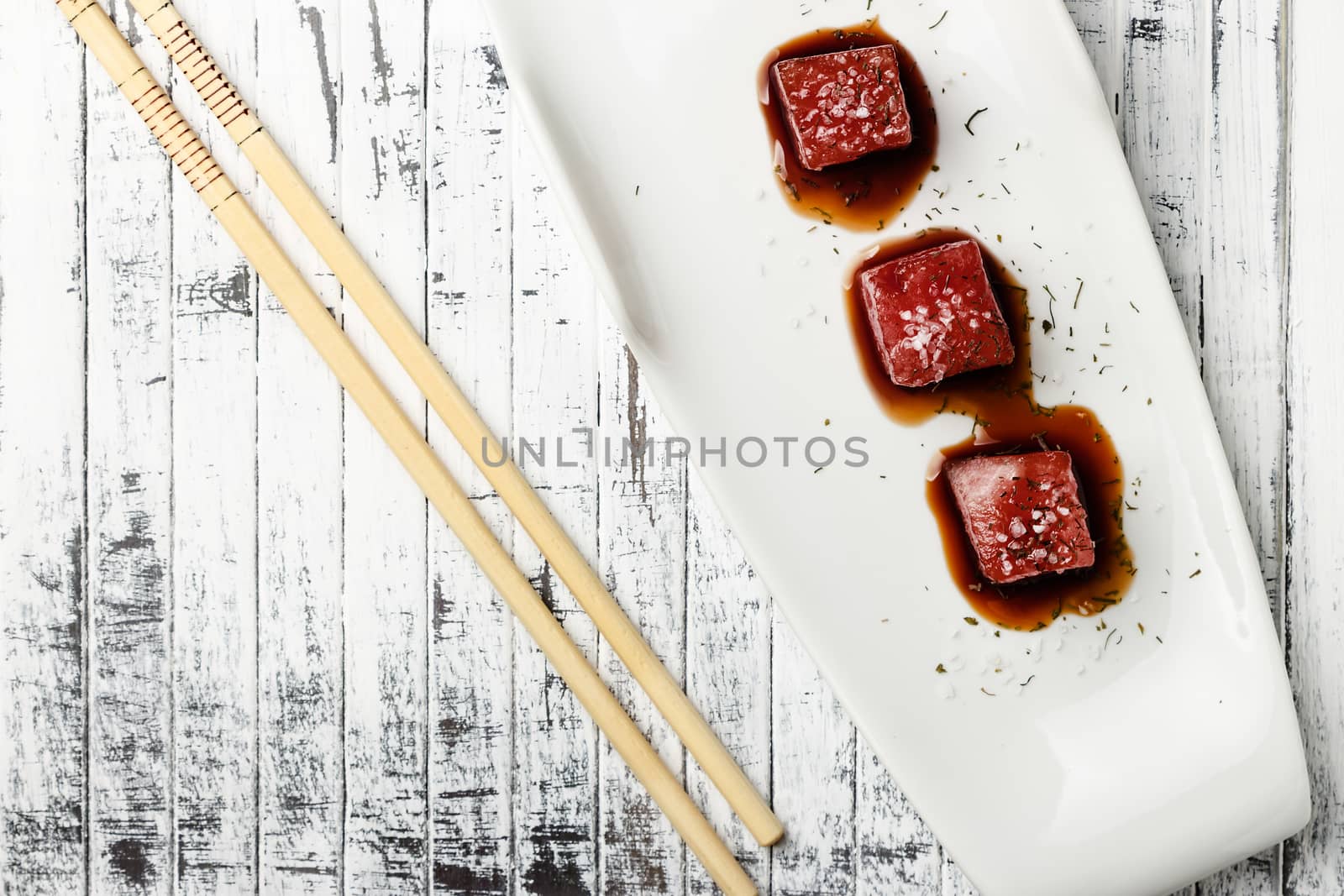 Tuna sashimi dipped in soy sauce,  thick salt and dill on old white wooden board with chopsticks. Viewed from above. Raw fish in traditional Japanese style. Horizontal image.