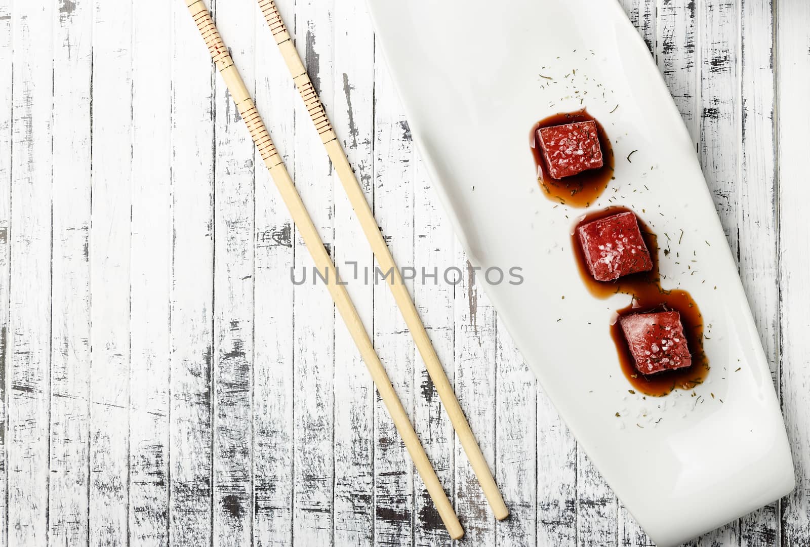 Tuna sashimi dipped in soy sauce,  thick salt and dill on old white wooden board with chopsticks. Viewed from above. Raw fish in traditional Japanese style. Horizontal image.