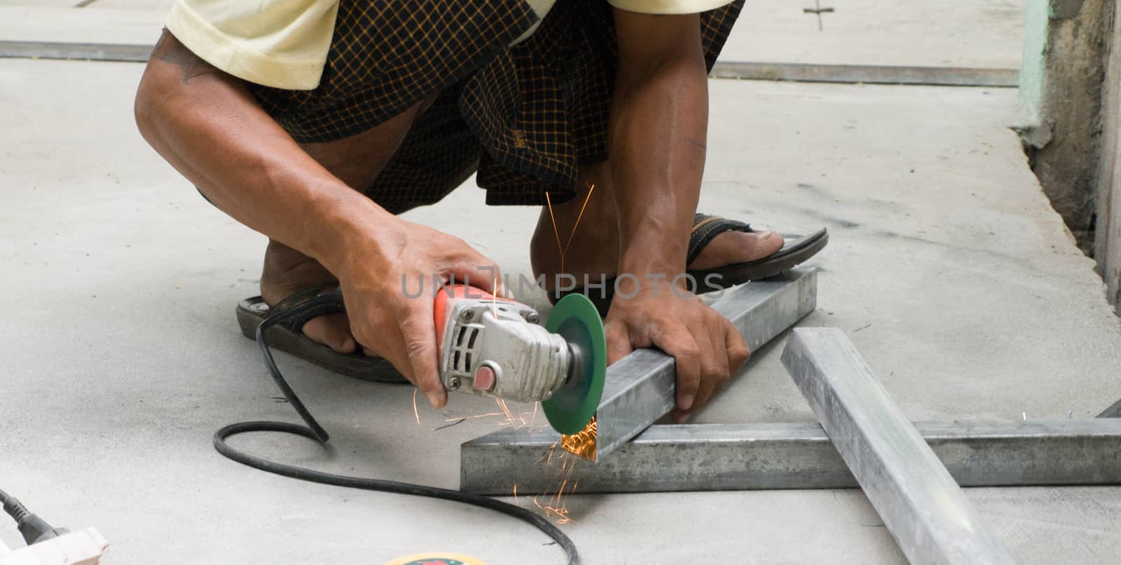 COLOR PHOTO OF WORKER CUTTING STEEL WITH ELECTRIC WHEEL GRINDER