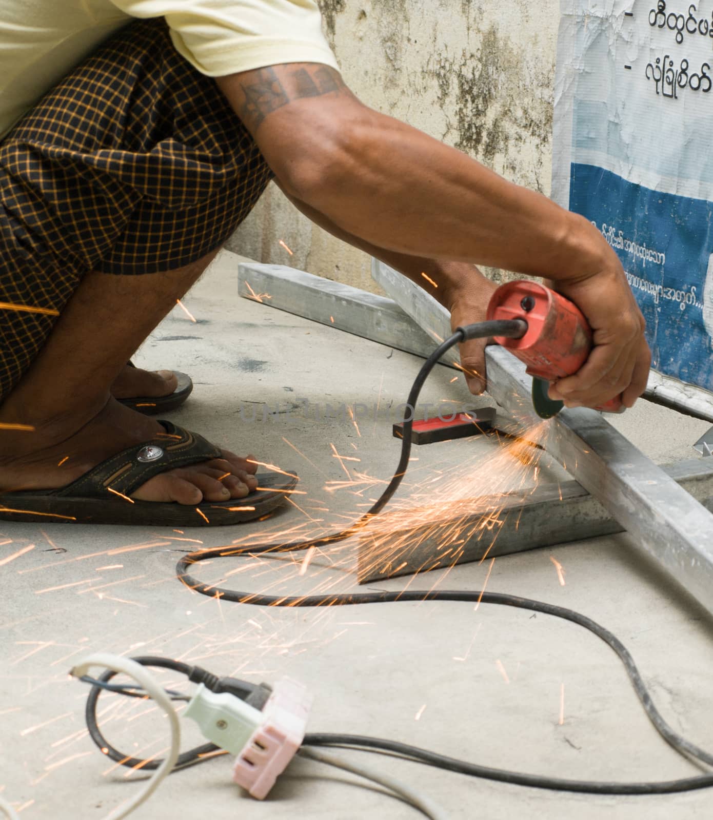 COLOR PHOTO OF WORKER CUTTING STEEL WITH ELECTRIC WHEEL GRINDER