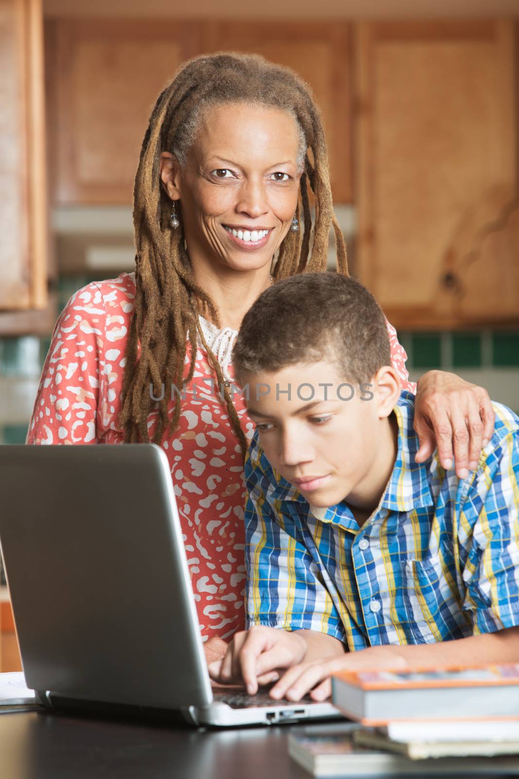 African-American mother and son work together on the computer in their kitchen