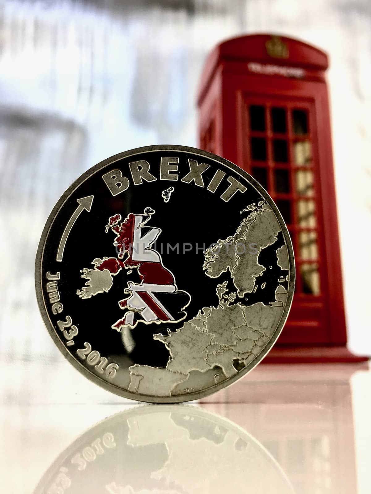 Physical silver brexit coin near red telephone box.