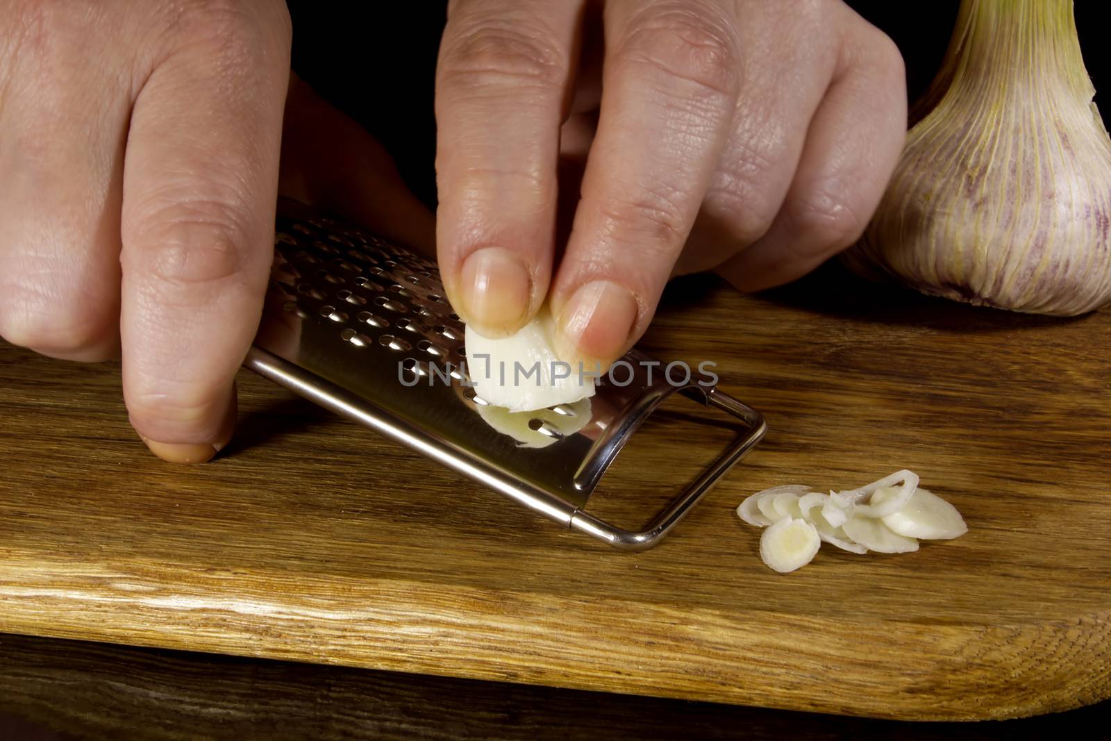 Female hands grind garlic on a grater on a black background