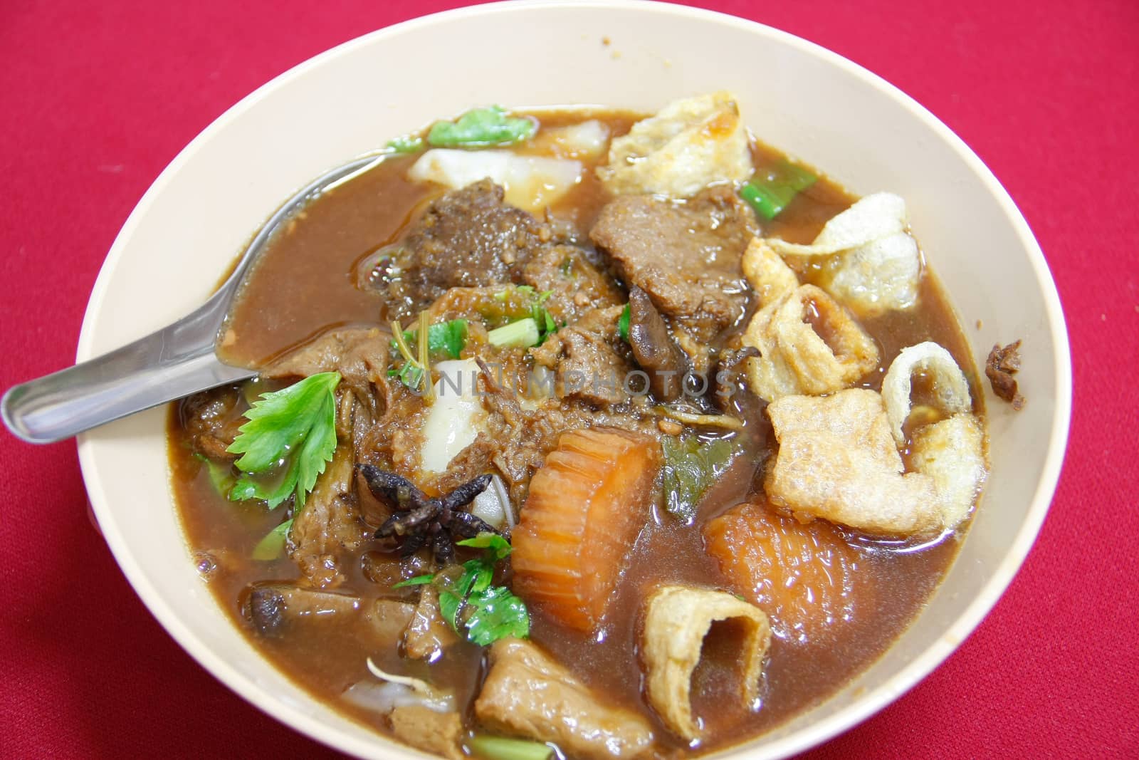 Thai style noodle soup with meat and vegetable in bowl on red floor