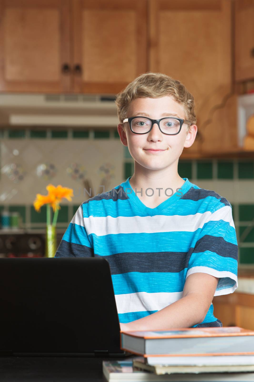 Cute smiling teenage male student in kitchen with books