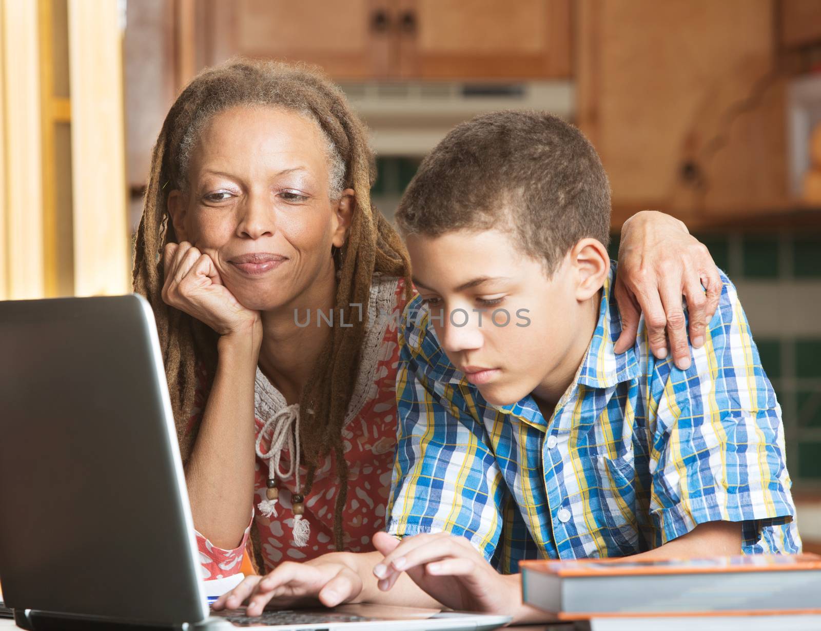 Mother and teen son work in kitchen on laptop by Creatista