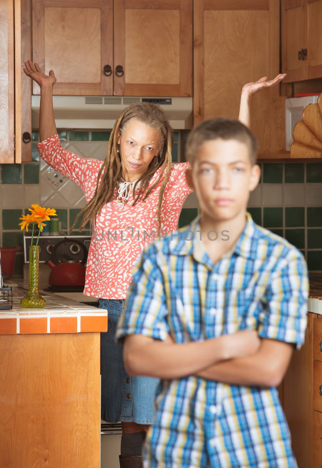 Mother of teenaged son throws her hands up in frustration as they both stand in the kitchen