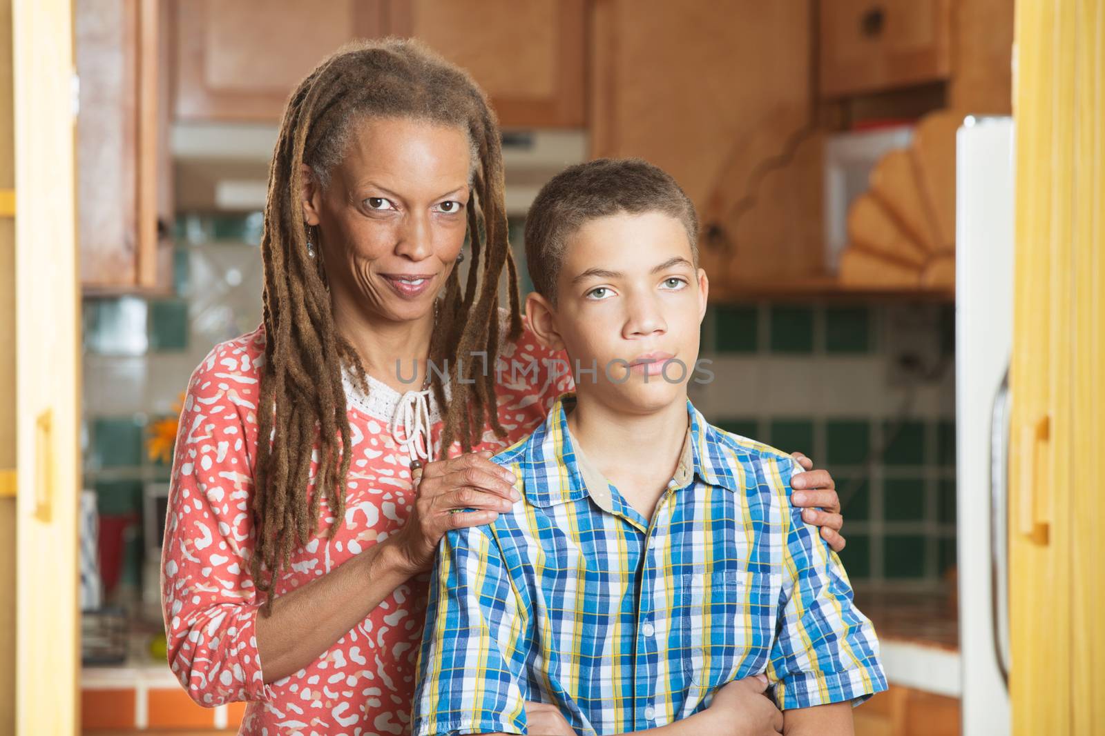 African-American mother and her frustrated teenaged son stand together in kitchen