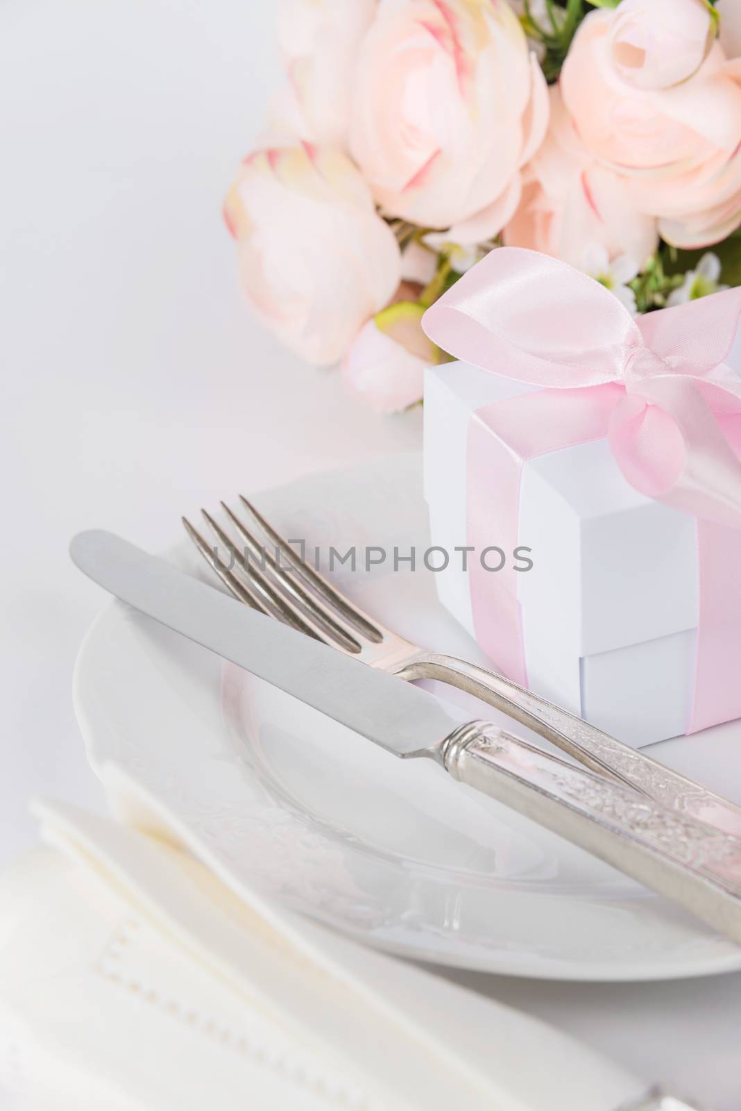 Beautiful decorated table with white plates, gift box with a pink ribbon, cutlery and pink flowers on white background, with space for text