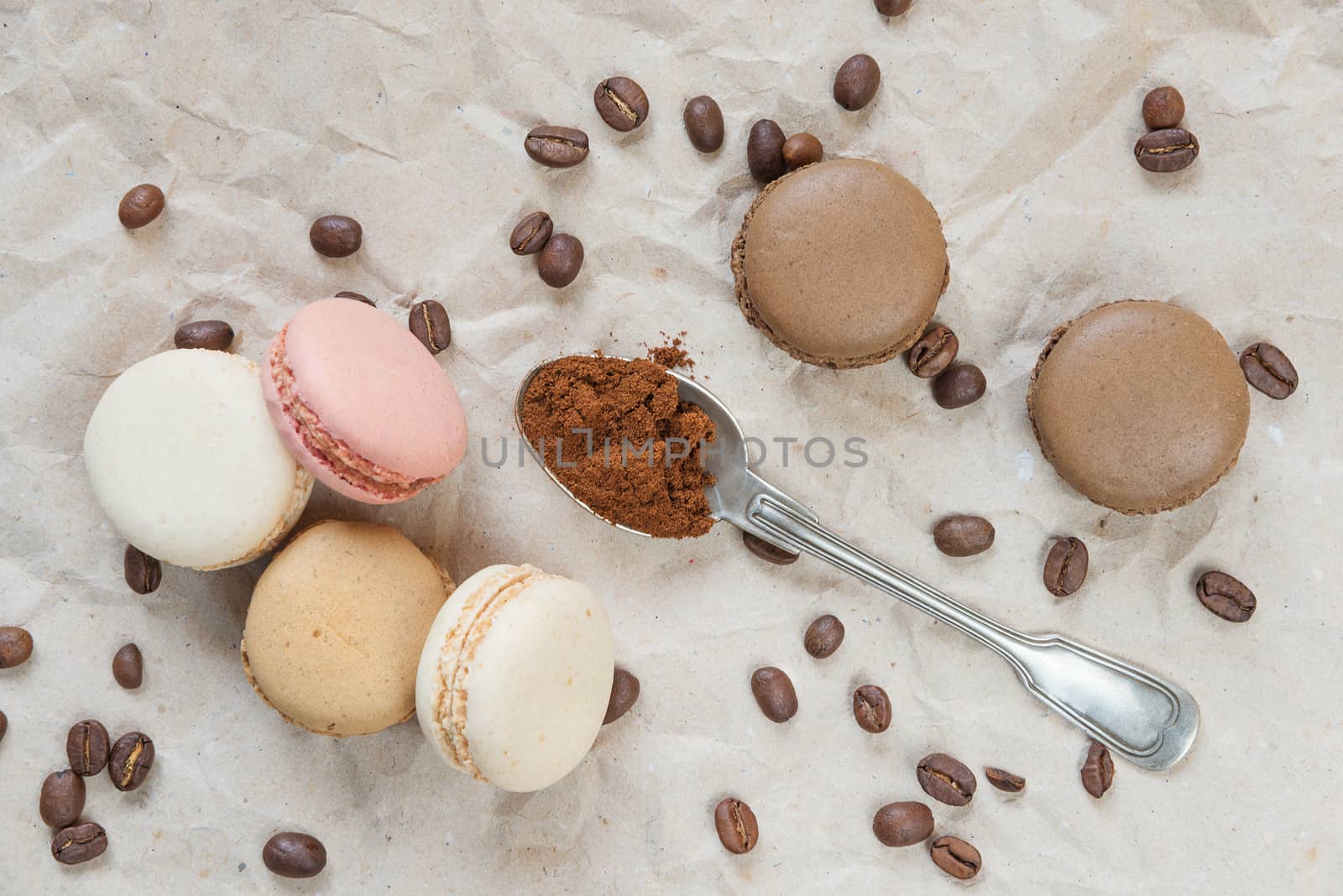 Multicoloured macaroons, coffee beans and ground coffee in teaspoon on the background of wrapping paper; top view, flat lay