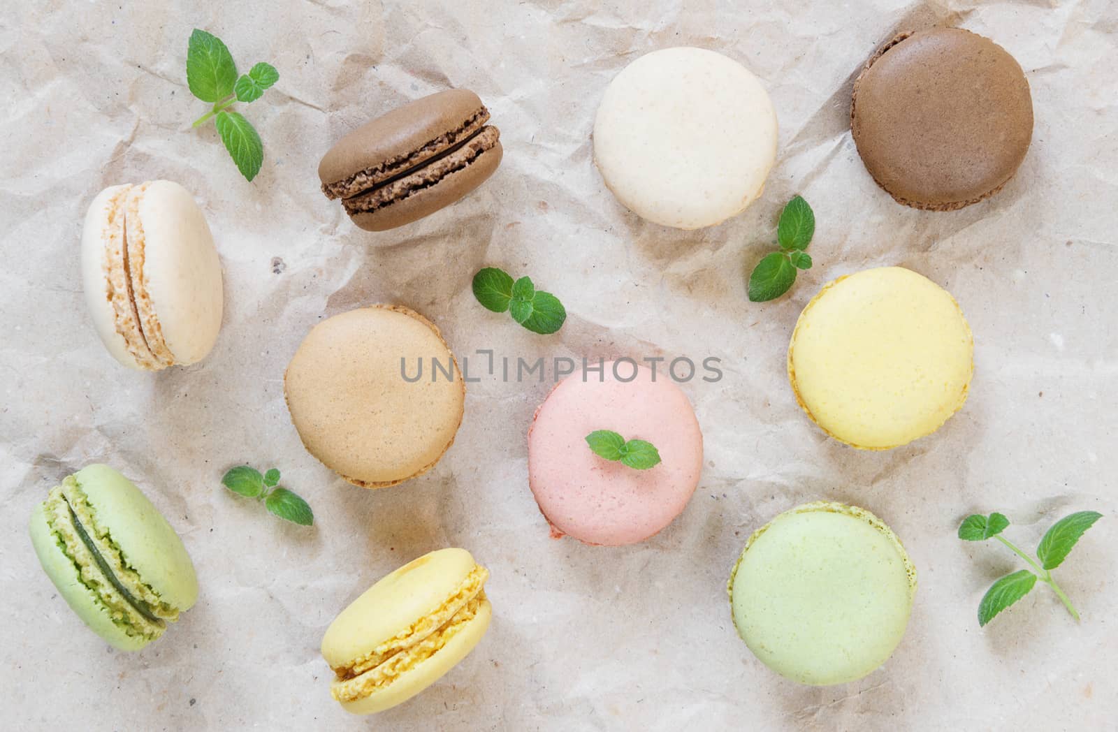 Multicoloured macaroons and green mint leaves on the background of wrapping paper; top view, flat lay