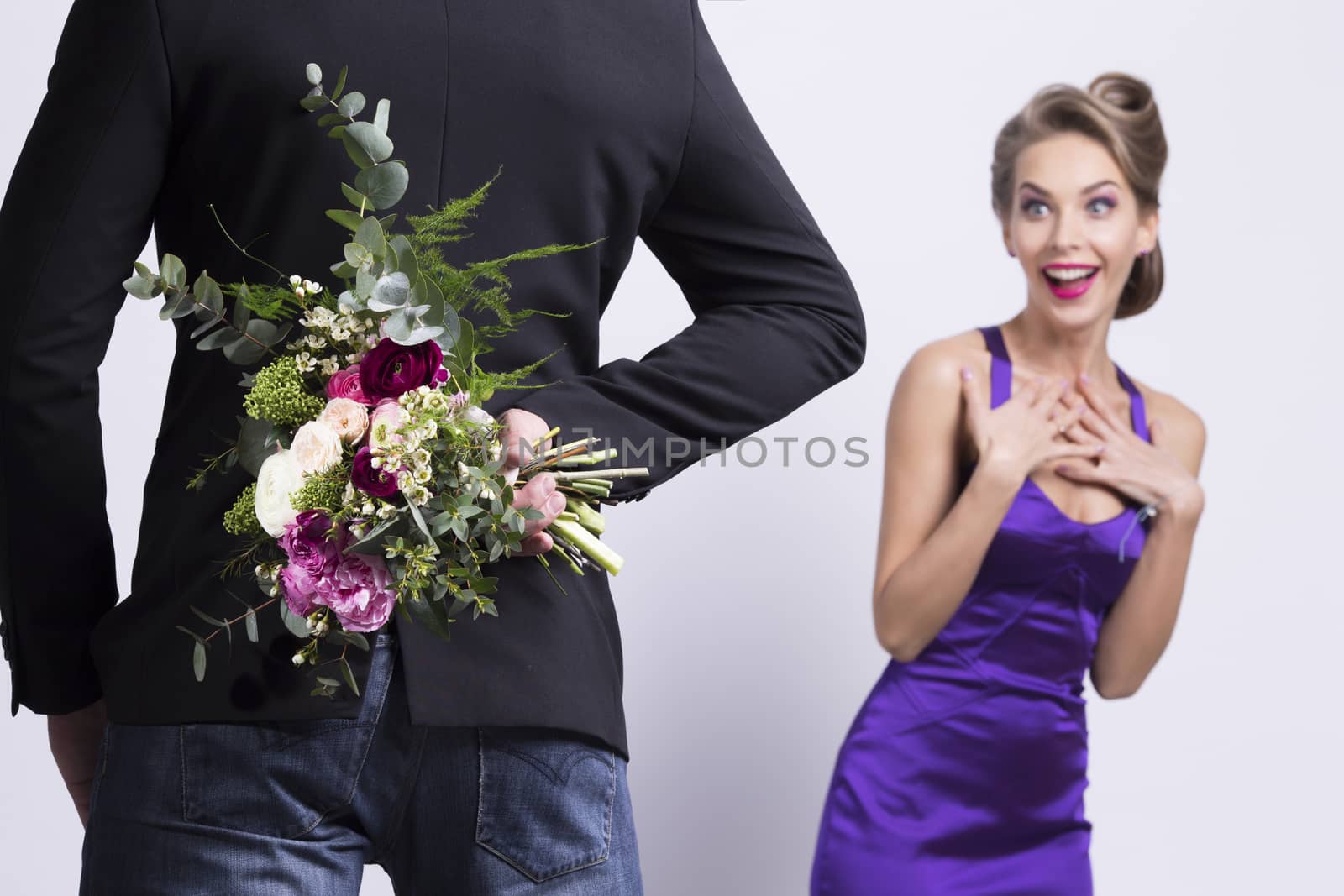 Man brings flowers to woman and hiding them behind back, womanin evening dress is surprised and happy